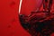 Red wine pouring with splashes on red background closeup. Glass of wine, drink for celebrating, date, family dinner, party. Wine