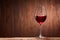 Red wine in the pure elegant wineglass standing on a wooden stand against wooden background.