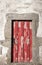 Red wooden aged door in stone wall. Ancient abandoned building. Medieval rustic architecture.