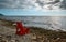 Red wooden armchair on a stone wild beach against the background of the sea and sky, the sun is hidden in the clouds. Seaside,