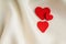 Red wooden decorative hearts on white silk background.