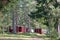 Red wooden finnish cabins cottages in green pine forest near river. Rural architecture of northern Europe