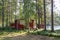 Red wooden finnish cabins cottages in green pine forest near river. Rural architecture of northern Europe