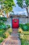 Red wooden gate with pergola and white fence of home with pathway in the garden