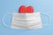 Red wooden heart covered with a white medical protective mask on a wooden light blue background