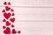 Red wooden hearts on the left border on a pink wooden background