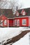 Red wooden houses with white windows during a snowy winter or spring. Snow is melting, showing a dirty ground underneath