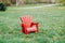 red wooden plastic muskoka Adirondack chair standing on green grass among yellow dandelion flowers in park outside
