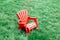 Red wooden plastic muskoka Adirondack chair standing on green grass among yellow dandelion flowers in park outside