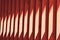 Red wooden slats. Abstract pattern with vertical lines and sunlight. Part of a bench, an element of building decor