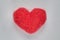 Red wool felted heart lying on white sheet close up