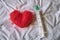 Red wool felted heart and a syringe lying on a white crumpled sheet. Top view