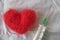 Red wool felted heart and a syringe lying on a white crumpled sheet. Top view