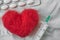 Red wool heart , an injection syringe and a tablet blister lying on a white crumpled sheet