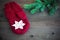 Red wool mitten with wiht cotton crocheted snowflake near green christmas fur tree on the rustic wooden background. Toned. Christm