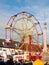 Red and yellow carousel wheel outside with people below blue sky