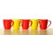 Red and yellow mugs in a row on wooden table. White background