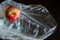 Red yellow ripe whole apple with green small leaf in a cellophane plastic bag on a wooden dark brown table. Top view.