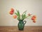 Red And Yellow Tulips In A Green Vase On A Wood Surface With Neutral Background