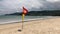 A red and yellow warning flag flutters in the wind on the beach