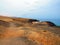 Reddish and arid volcanic coastline contrasts with the blue of the ocean. Desert and extreme landscape. Natural space, mountains