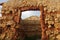 reddish brown brick stone structure with beige clay and a giant gateway . some blue sky can be seen through the door.