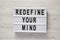 `Redefine your mind` words on lightbox over white wooden surface, top view. Overhead, flat lay