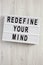 `Redefine your mind` words on lightbox over white wooden surface, top view. Overhead, flat lay