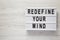 `Redefine your mind` words on lightbox over white wooden surface, top view. Overhead, flat lay, from above