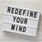 `Redefine your mind` words on modern board over white wooden surface, top view. Overhead, flat lay