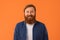 Redhaired bearded man stands smiling to camera against orange background