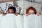 Redhaired ginger caucasian happy female and multi-ethnic afro man together lying in bed bedroom hiding under the blanket
