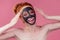 Redhaired ginger teenager girl with black clay mask on her pretty face on pink studio background