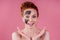 Redhaired ginger teenager girl with black clay mask on her pretty face on pink studio background