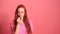 Redhaired ginger woman in pink studio background picks his nose finger