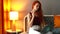 Redhaired ginger woman sitting at her bedroom with laptop on the bed , evening lamp on