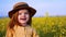 Redhead baby girl in boater hat enjoys the blooming canola field at sunny spring day