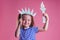 Redhead blonde charming female kid celebration independence holding a paper torch and diy crown on a pink background in