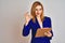 Redhead business caucasian woman holding clipboard over isolated background doing ok sign with fingers, excellent symbol