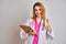 Redhead caucasian doctor woman wearing pink stethoscope and holding clipboard happy with big smile doing ok sign, thumb up with