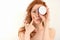 Redhead girl with clean skin looking at the camera, closing eye with a jar of cream, burying finger on neck, stretching