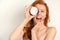 Redhead girl with clean skin in a towel looks at the camera, closing one eye with a jar of cream and laughs, putting