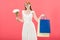 Redhead girl in glasses and white dress holding bouquet of flowers and shopping bags isolated on pink