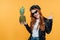 Redhead girl in leather jacket posing with pineapple and showing rock sign isolated on yellow.