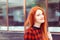 Redhead girl looking at the camera, smiles to somebody outdoors in red black squared shirt