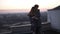 Redhead guy whirls his girlfriend on the roof with a cityscape and sunset horizon on the background. Happy time together