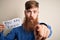 Redhead Irish business man with beard holding paper with you are fired text pointing with finger to the camera and to you, hand