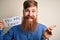Redhead Irish business man with beard holding paper with you are fired text very happy pointing with hand and finger to the side