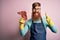 Redhead Irish butcher man with beard holding raw beef steak over pink background surprised with an idea or question pointing