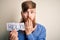 Redhead Irish man with beard holding paper with help message over blue background cover mouth with hand shocked with shame for